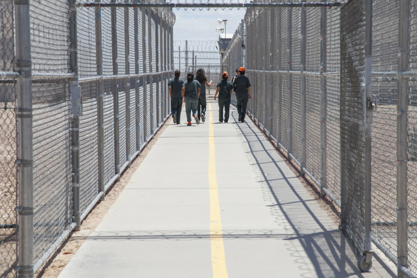 Group of people walking together in a fenced and gated ICE detention center.