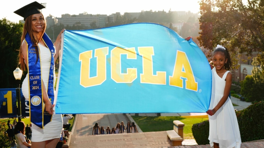 Schinal Harrington holds up a UCLA flag on her graduation day with her young daughter.