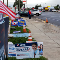 Man in orange hat on street with many campaign signs