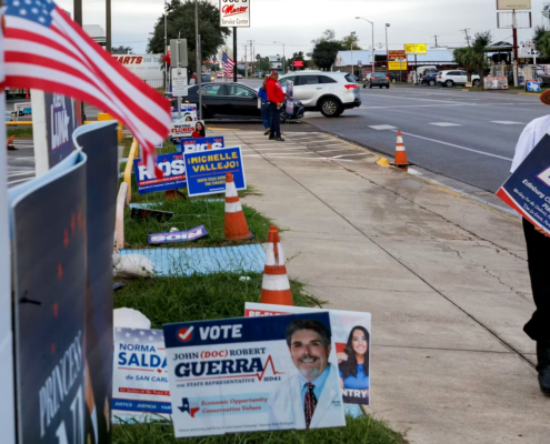 Man in orange hat on street with many campaign signs