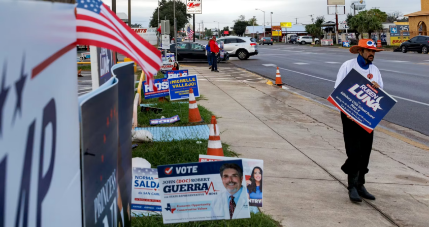 Man in orange hat on street with many campaign signs