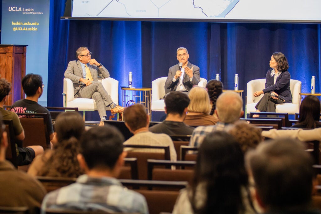 3 panelists speak in front of an audience on stage.|||