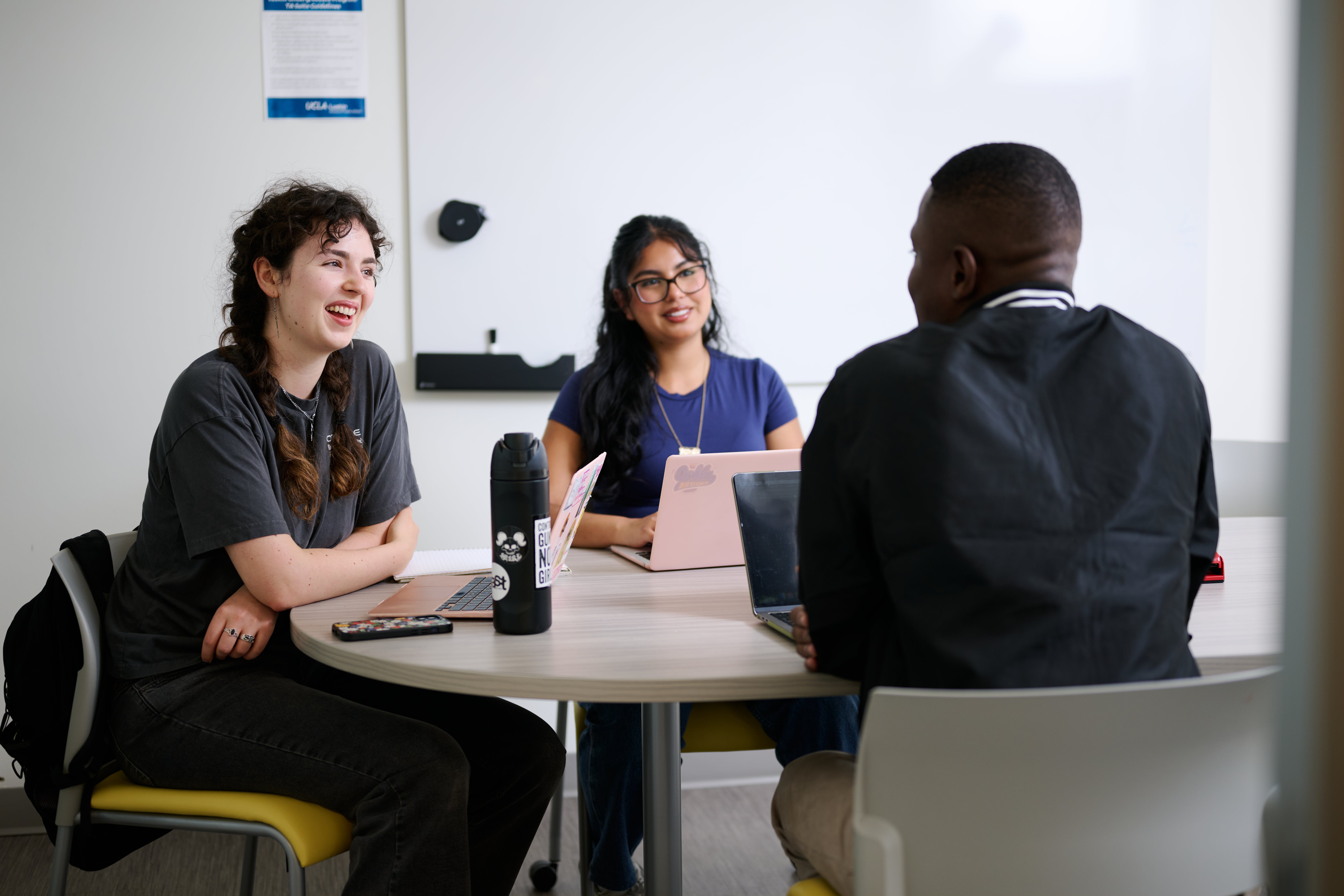 3 Students smiling and having a group discussion around a table at UCLA Luskin