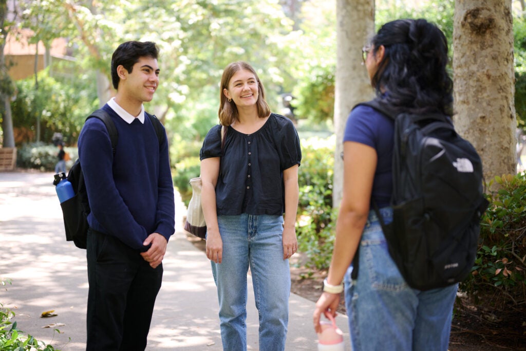 Three students stand in the Sculpture Garden at UCLA speaking to each other
