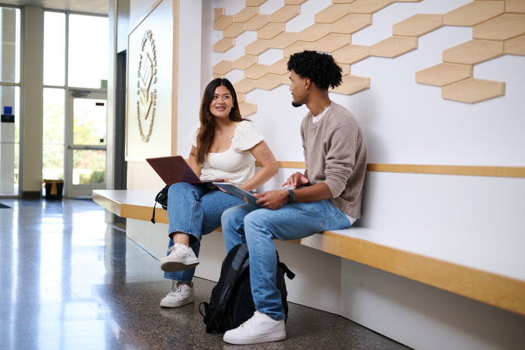 Two student sitting inside an academic foyer chatting