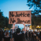 a photo of a protest with one person holding up a cardboard sign that reads No Justice No Peace