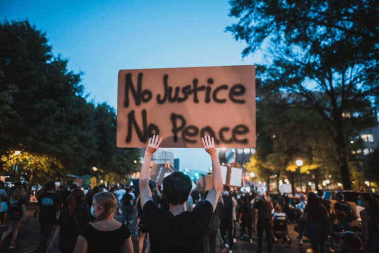 a photo of a protest with one person holding up a cardboard sign that reads No Justice No Peace