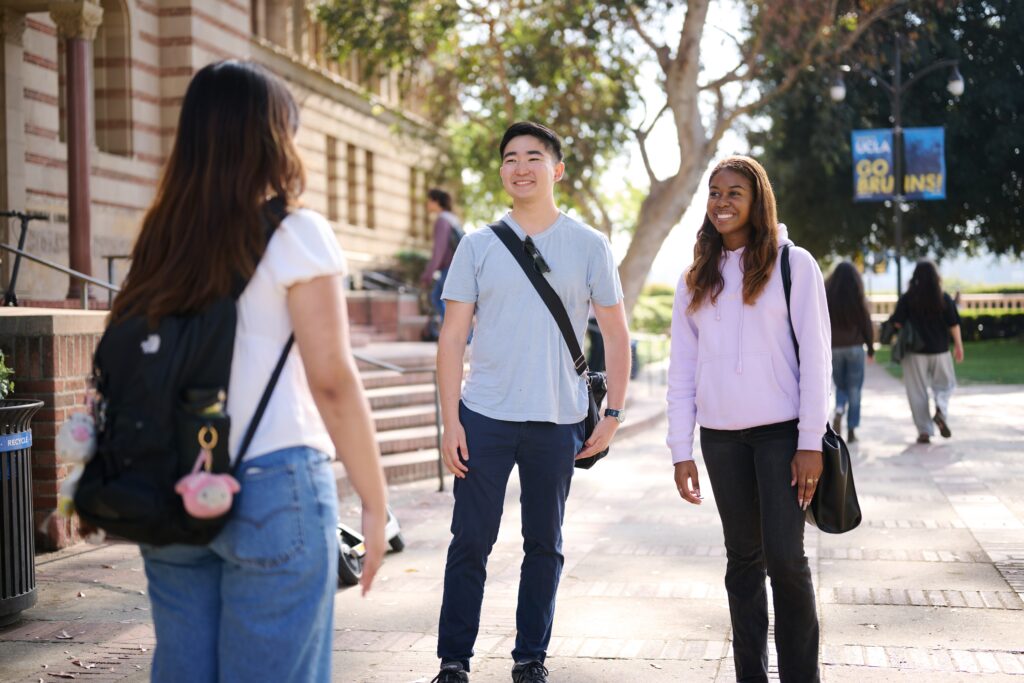 One student has back towards the camera and two students smile at her, in front of Royce Hall at UCLA