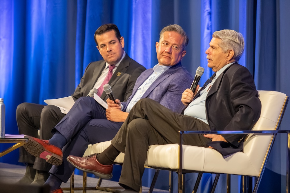 three men in suits sitting on stage