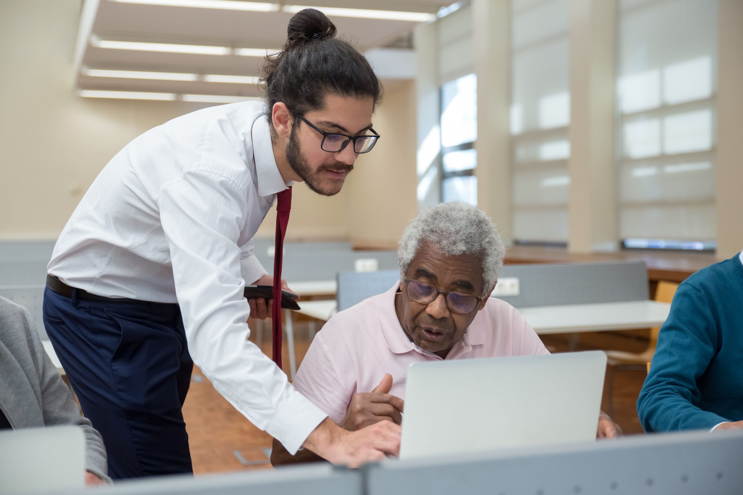 A young man helps a senior citizen in a classroom setting