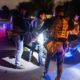 Immigration enforcement officers handcuff a man in the night, in front of a car in the middle of the road.