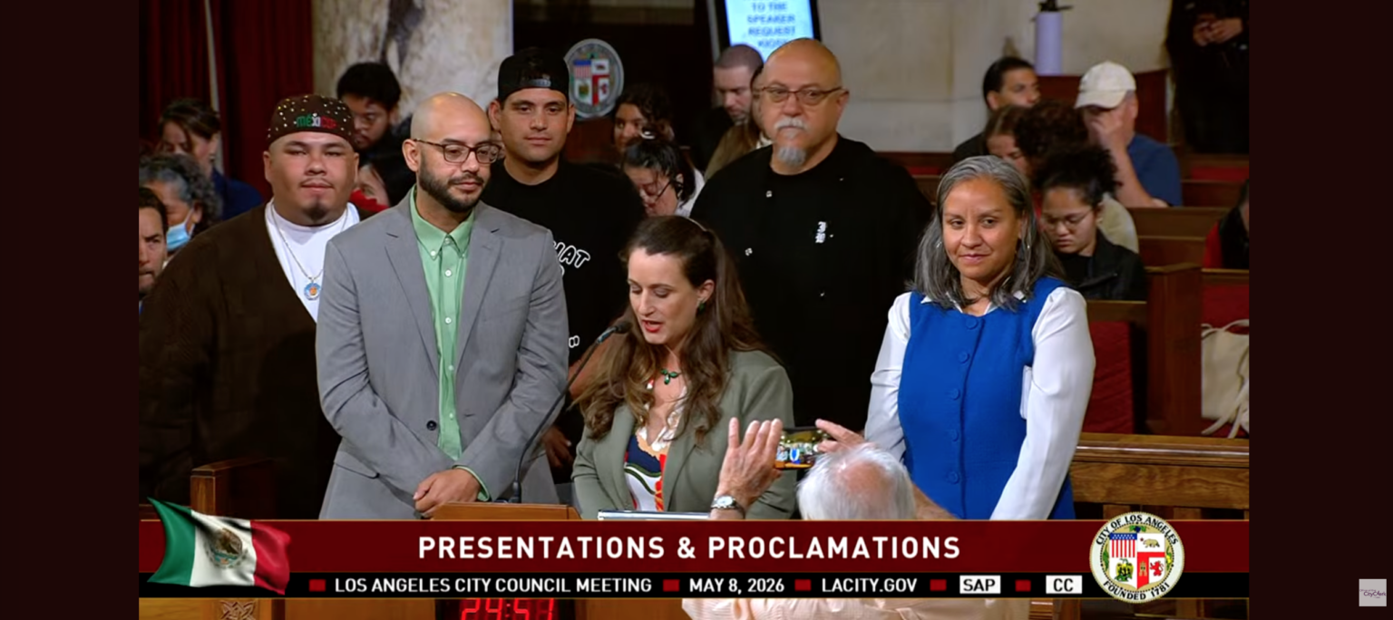 Los Angeles City Council Meeting on May 8, a speaker presents José Loya and Amada Armenta with their "impactful chicanos" award at City Hall.|Two photos next to each other, on the left is Jose Loya and Amada Armenta holding up their "Impactful Chicanos" awards inside City Hall, the photo on the right is of Jose and Amada standing next to a framed illustration of UCLA Latino Policy and Politics Institute.