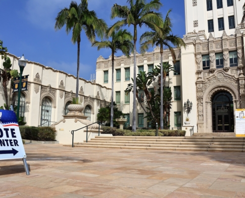 Vote center sign in front of ornate building and palm trees