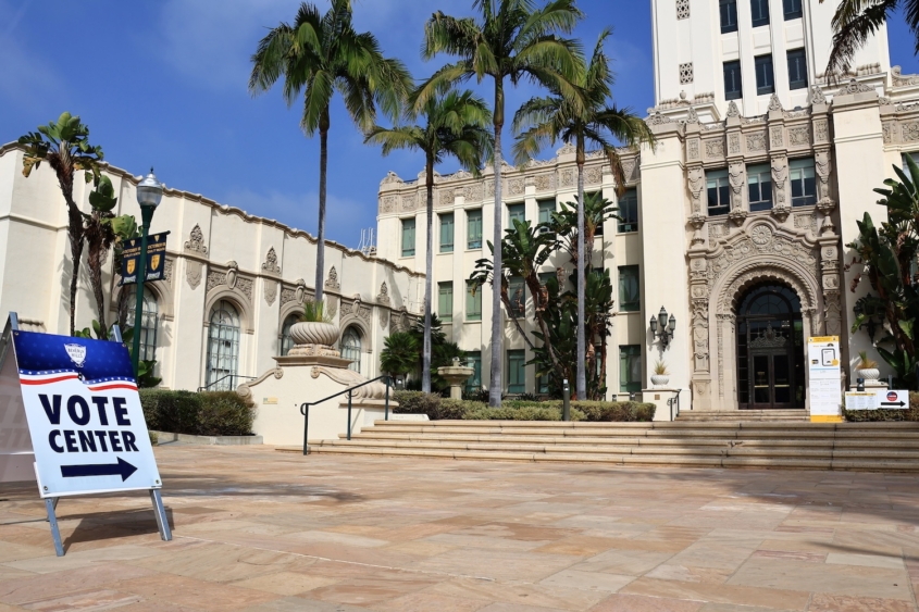 Vote center sign in front of ornate building and palm trees