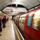 Passengers wait in the subway station for the train, blurry photo of a subway train moving on the right while passengers stand on the left.