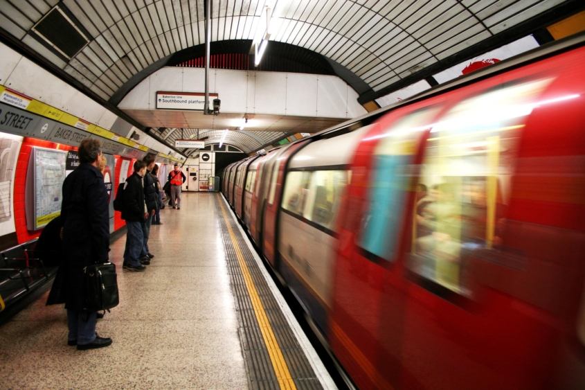 Passengers wait in the subway station for the train, blurry photo of a subway train moving on the right while passengers stand on the left.