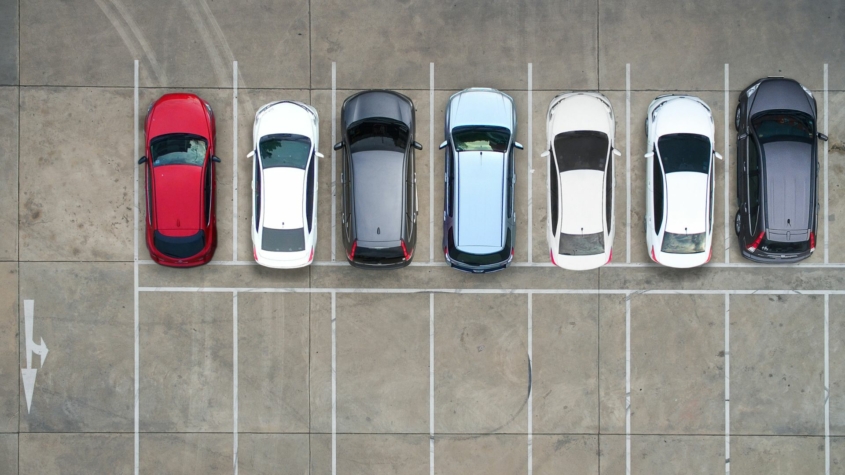 Aerial view of a parking lot with a row of cars and another row of empty parking spaces.