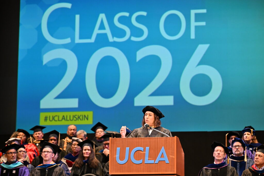 Caroline Menjivar speaks on stage at UCLA Luskin Commencement ceremonies on June 12, 2026. She is a California State Senator and a prominent alumna of the UCLA Luskin School of Public Affairs, having earned her Master of Social Welfare (MSW) in 2018.|Jacqueline Waggoner '18 on the stage in front of a podium giving her commencement speech to the undergraduate class of 2026.