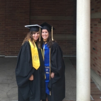 MSW Alumni Emily Dillon graduate of 2016 class, stands with her female friend, both are in cap and gown at UCLA graduation in front of a brick building.