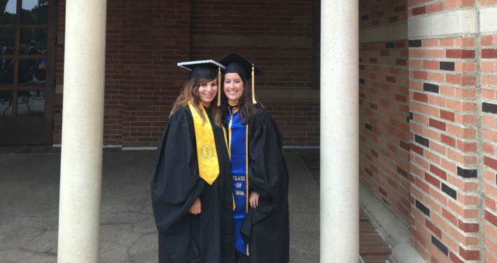 MSW Alumni Emily Dillon graduate of 2016 class, stands with her female friend, both are in cap and gown at UCLA graduation in front of a brick building.