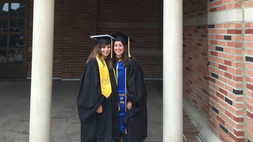 MSW Alumni Emily Dillon graduate of 2016 class, stands with her female friend, both are in cap and gown at UCLA graduation in front of a brick building.