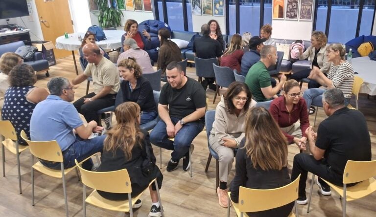 Visiting educators sit in concentric circles for one-on-one conversations|Woman holds small art collage with lyric "there is a crack in everything, that's how the light gets in."|Large group of people pose outdoors|Group works on art project on outdoor patio|Man in glasses delivers lecture