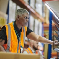 African American female warehouse worker wearing an orange vest doing her job.