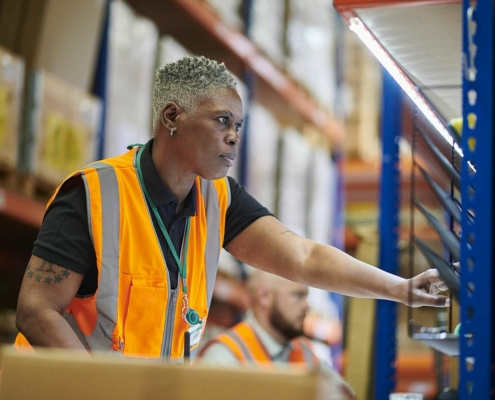 African American female warehouse worker wearing an orange vest doing her job.