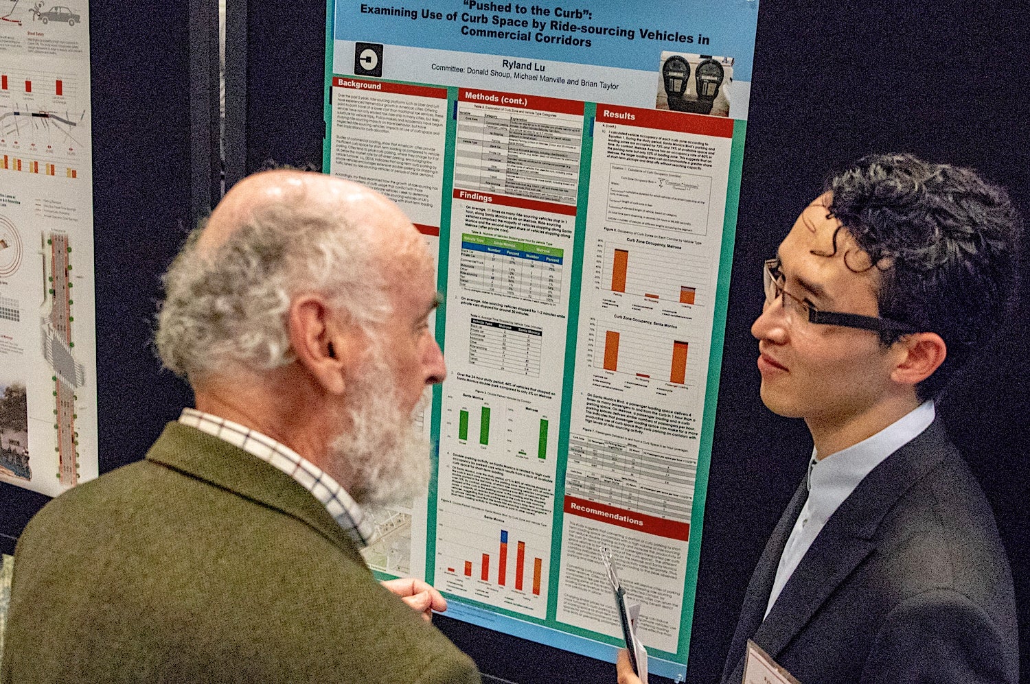 gray-haired bearded man with student and poster board