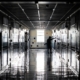 Dimly lit hallway of a high school, with lockers on either side, a man stands with his arms out touching a wall, conveying sadness.
