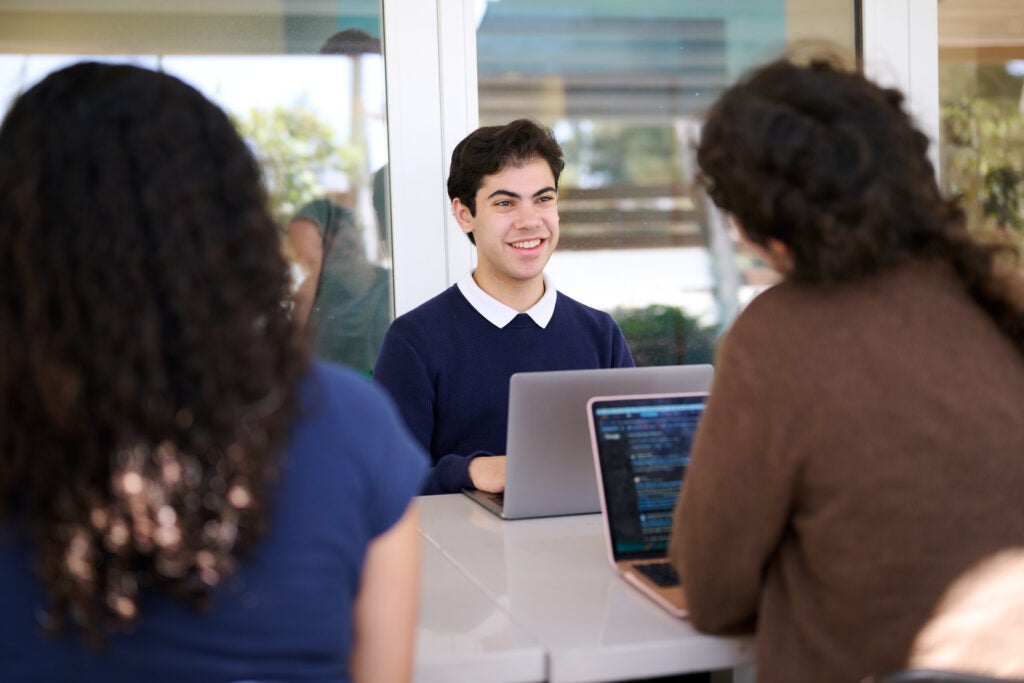 one student sits and faces two students who have their back go the camera, smiling and talking at UCLA