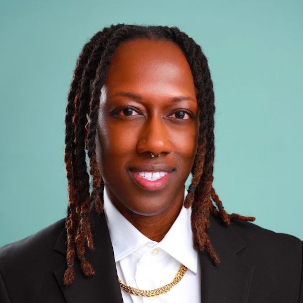 headshot of person with white shirt, black blazer and gold chain