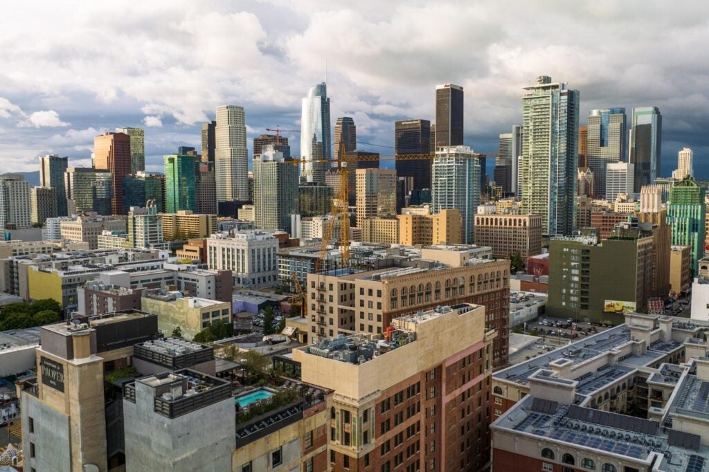 This photo captures the dense skyline of Downtown Los Angeles, featuring iconic skyscrapers like the U.S. Bank Tower and a prominent yellow construction crane.