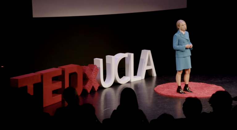 Kelly Turner TedXUCLA talk screenshot with her on a black stage in a blue blazer and skirt.