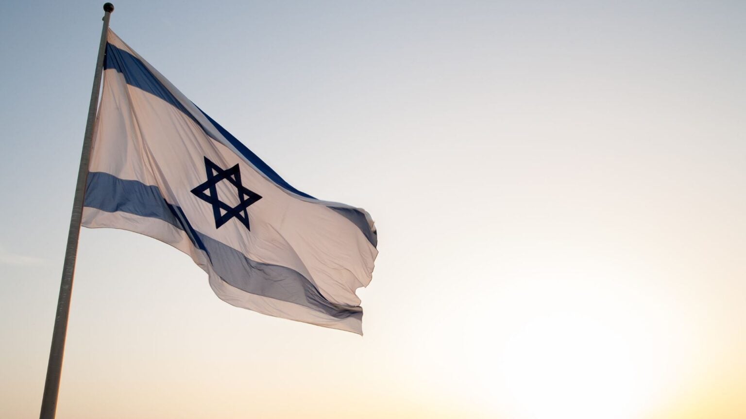 Photo looking up a flying flag of Israel, background is the sky