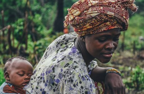 Woman bends down carrying a sleeping baby on her back