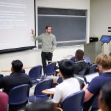 Professor pointing at screen in front of classroom