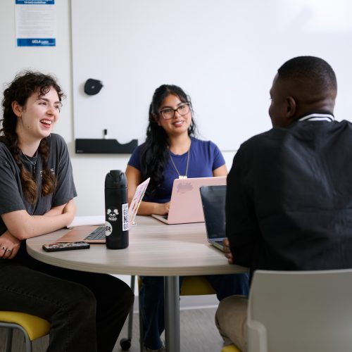 3 Students smiling and having a group discussion around a table at UCLA Luskin