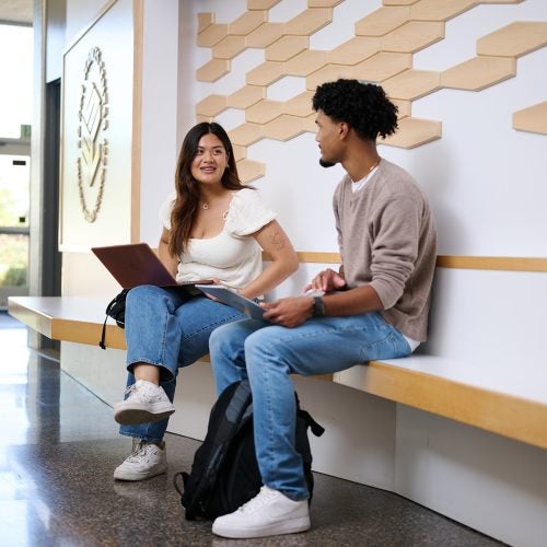 Two student sitting inside an academic foyer chatting