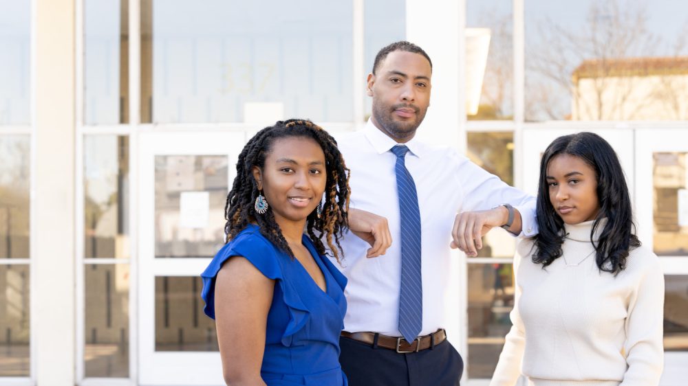 Three students in front of glass entryway