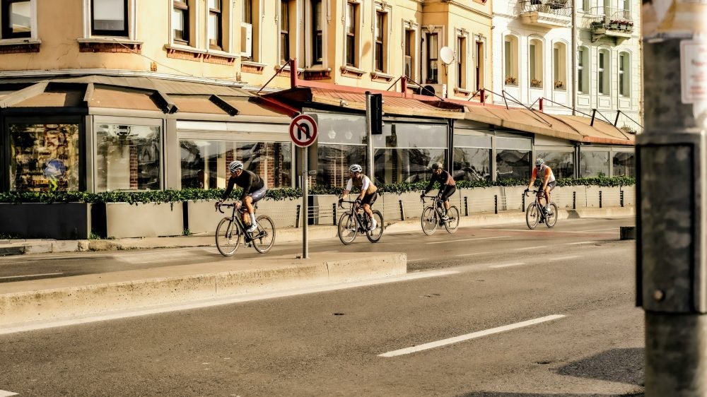 4 men biking cycling in a line on a street in a city