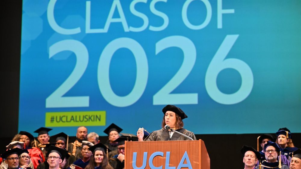 Caroline Menjivar speaks on stage at UCLA Luskin Commencement ceremonies on June 12, 2026. She is a California State Senator and a prominent alumna of the UCLA Luskin School of Public Affairs, having earned her Master of Social Welfare (MSW) in 2018.|Jacqueline Waggoner '18 on the stage in front of a podium giving her commencement speech to the undergraduate class of 2026.