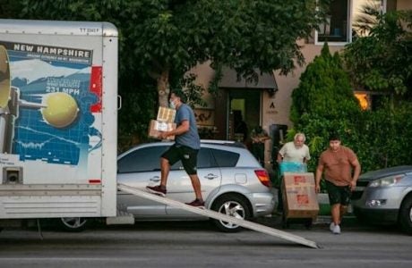 Man carriers cardboard boxes into the back of a Uhaul truck parked in front of a house