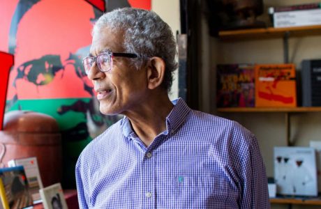 Middle-ahed man wearing glasses and a button-down shirt looks away from the camera in a bookstore.