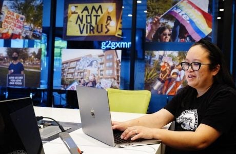 Woman at laptop computer in front of wall of poster