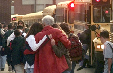 school crowd including woman in red coat hugging two girls in front of school bus
