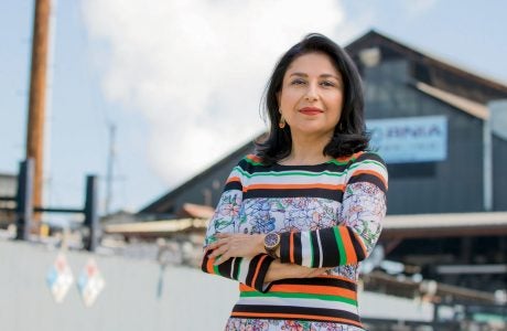 woman stands with arms crossed in foreground and building in distance