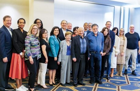 Board members gather after a meeting for a group photo|Portrait image of person in patterned white shirt|Close-up photo of person with black hair and hoop earrings|group photo of several people taken during tour of Venice Family Clinic.