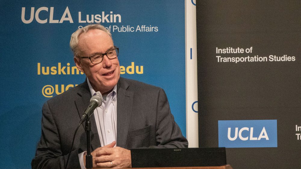 Man in glasses at podium with blue and black backdrop|