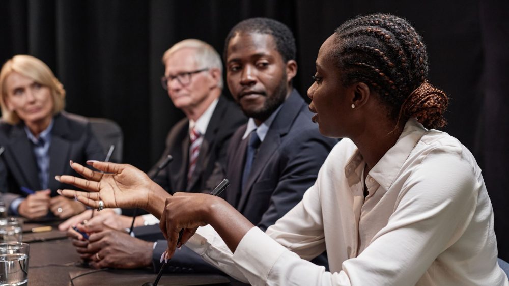 Black Woman Posing Question to Colleague during Committee Session at Political Meeting|Police officer and driver.